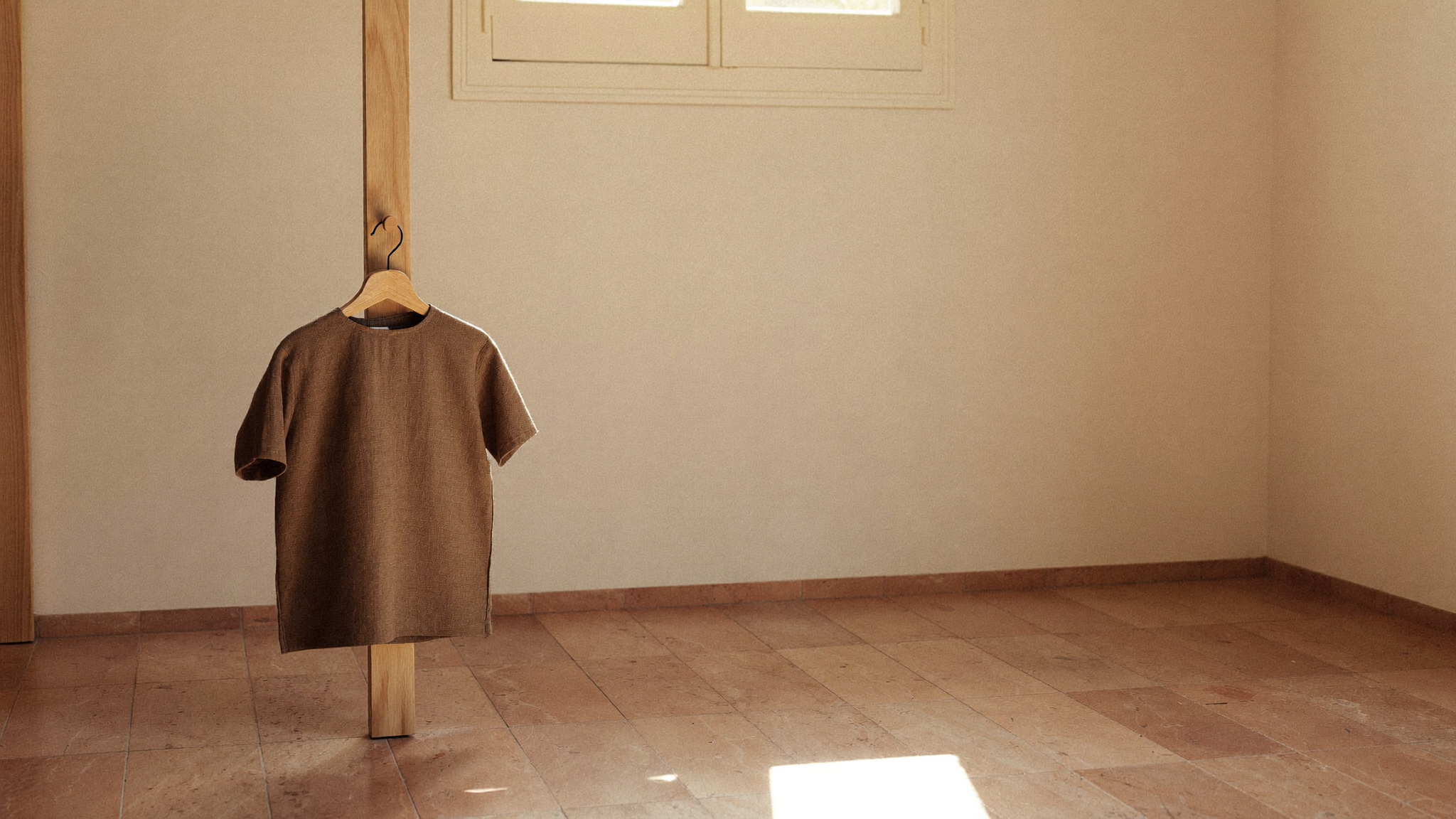 Leerer, sonnendurchfluteter Winkel eines minimalistischen Schweizer Kinderzimmers mit einem einzelnen Leinen-Kleidungsstück an einem schlanken Eichenhaken